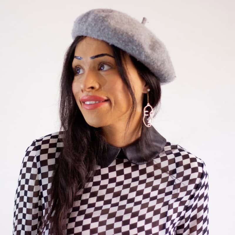 Fashionable woman wearing a checkered shirt and a gray beret, smiling and looking to the side.